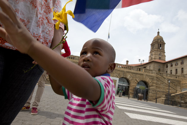 A father and his son holding a South African flag prepare to lay flowers at a makeshift memorial at the Union Buildings in Pretoria, South Africa, Saturday Dec. 7, 2013, where preparations are underway for Nelson Mandela to lie in state for three days prior to burial in his hometown of Qunu. South Africa is readying itself for the arrival of a flood of world leaders for the memorial service and funeral of Nelson Mandela as thousands of mourners continued to flock to sites around the country Saturday to pay homage to the freedom struggle icon. (AP Photo/Peter Dejong)